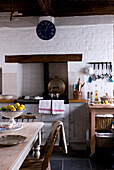 Country style kitchen with Aga and white painted brick wall with clock