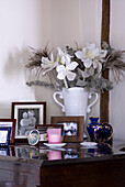 Detail of white vase with fake flower arrangement and family photos on top of a piano