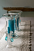 A delicate French grey quilted table runner with hurricane lamps and crystal droplet candle holders adorned with turquoise candles