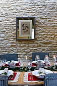 Artwork on exposed stone wall of Wiltshire farmhouse with dining table set for Christmas dinner