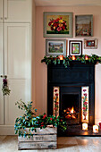 Crate of holly by lit tiled fireplace with artwork display