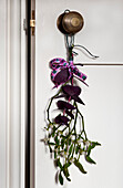Purple flowers and mistletoe hang from brass door handle
