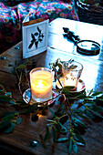 Lit candles and greetings card with magnifying glass and greenery on coffee table at Christmas