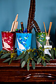 Art equipment in pencil holders with eucalyptus on wooden mantlepiece