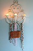 Beaded bag and necklaces hang on wall mounted candle holder