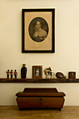 Wooden casket below shelf with ornaments and family portrait