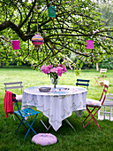 Summer garden table setting under a tree with paper lanterns hanging in a tree