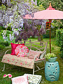 Bench with cushions and throws in a summer garden with purple wisteria and a parasol