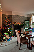 Beleuchtetes Feuer und bunt geschmückter Weihnachtsbaum im Esszimmer eines Hauses in London UK