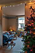 Christmas tree with lit fairylights and view through doorway to living room of London home UK
