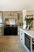 Black range oven in flagstone kitchen with pastel green fitted units in kitchen of Canterbury home England UK