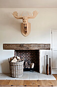 Carved wooden stags head mounted above exposed brick fireplace with log basket in Canterbury home England UK