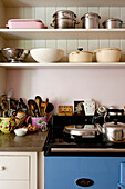 Kitchenware and utensils on open shelving with kettle on oven in London home UK