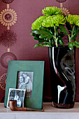 Vase of green Chrysanthemum flowers with black and white family photographs on mantlepiece in London home UK
