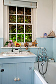 Wash basin and shower fitting at window of bathroom with light blue paintwork in London home UK