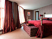 Curtains in window of red velvet bedroom with patterned blanket box in London apartment England UK