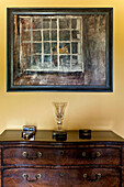 Artwork above wooden chest of drawers in rural Suffolk home England UK