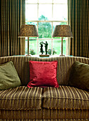 Red cushion on sofa with matching gold metallic lamps and statue of couple dancing in rural Suffolk home England UK