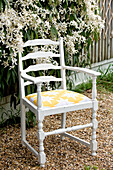 Re-upholstered chair on gravel with floral blossom in garden of London home, UK