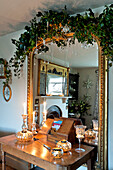 Silver candle holders on wooden table with gilt framed mirror and floral garland in Walberton home, West Sussex, England, UK