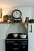 Saucepans on recessed hob below clock and shelf with Christmas garland in Walberton home, West Sussex, England, UK