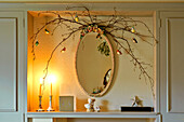Twig arrangement and oval shaped mirror with lit candles in Walberton home, West Sussex, England, UK