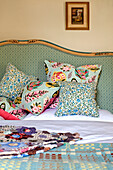 Floral and leaf patterned cushions on bed with patchwork quilt in Hertfordshire home, England, UK