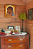 Books on wooden chest of drawers with religious artwork in Essex home, England, UK