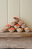 Homemade cupcakes on stone mantlepiece with yellow panelled wall in Buckinghamshire home, England, UK
