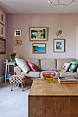 Kunstwerke über dem hellbraunen Sofa im rosa Wohnzimmer des Hauses der Familie Bovey Tracey, Devon, England, UK