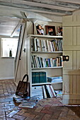 Bücherregal und Handtasche in gemauerter Eingangshalle eines Bauernhauses in Suffolk, England, Vereinigtes Königreich