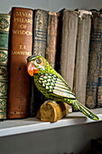 Painted parrot and hardback books on shelf of Suffolk farmhouse, England, UK
