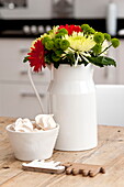 Red and yellow Chrysanthemums in white ceramic jug with meringues on table in Wadebridge home, Cornwall, England, UK