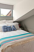Gestreifte Decke und Kissen mit dem Schriftzug 'SEA' auf dem Doppelbett unter dem Fenster in einem Haus in Wadebridge, Cornwall, England, UK