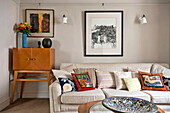 Variety of cushions on sofa with retro wooden cabinet in Padstow cottage, Cornwall, England, UK