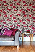 Pink cushions on silver sofa with rose patterned wallpaper in living room of Middlesex family home, London, England, UK