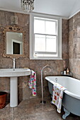 Decorative mirror above pedestal basin with freestanding roll-top bath in Middlesex family home, London, England, UK