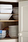 White ceramic crockery in cupboard of contemporary Suffolk/Essex home, England, UK