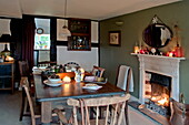 Esstisch und Stühle aus Holz mit beleuchtetem Feuer in einem Cottage in Shropshire, England, UK