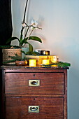 Lit candles and orchid on wooden chest of drawers in Shropshire cottage, England, UK