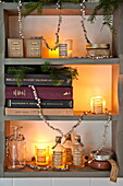 Lit candles and books on wall mounted shelf with Christmas decoration in Shropshire cottage, England, UK