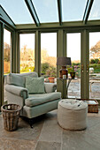 Light green armchair with footstool at conservatory doors of Sherford barn conversion Devon UK