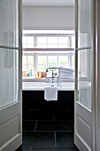 View of freestanding bath below window through glass paned double doors in Crantock home Cornwall England UK
