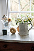 Cut flowers in ceramic jug with gold baubles at window in Crantock home Cornwall England UK