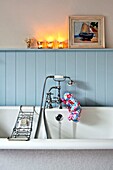 Beleuchtete Teelichter über einer hellblau getäfelten Badewanne mit Duscharmatur und Ablage in einem Einfamilienhaus in Penzance, Cornwall, England UK