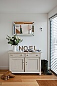 Cut flowers and single word 'NOEL' on sideboard with boots at entrance to Wadebridge home North Cornwall UK