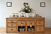 Storage jars on wooden sideboard with white roses in Wadebridge family home, North Cornwall, UK