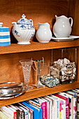 Recipe books and teapot with jugs on wooden kitchen shelves in modern home, Cornwall, UK