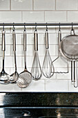 Metallic utensils hang on rail with white tiles in modern kitchen, Cornwall, UK