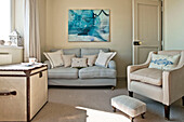 Cream armchair with light grey sofa and modern artwork in living room of family home Cornwall UK